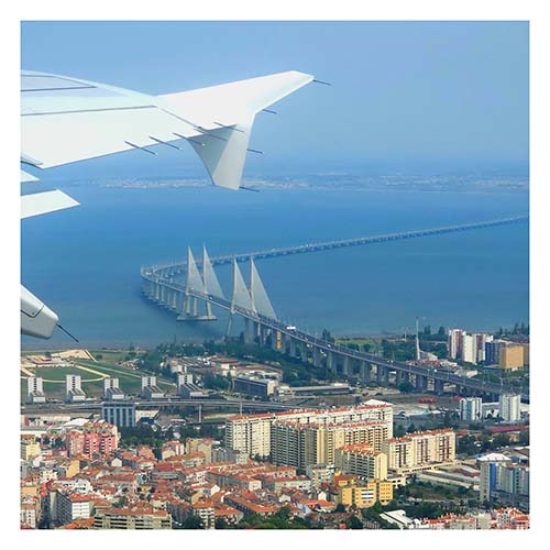 Blick aus einem Flugzeugfenster. Der Flügel ist rechts oben. Darunter ist Lissabon und der Atlantik. Vasco da Gama Brücke führt auf die andere Seite des Tajo.