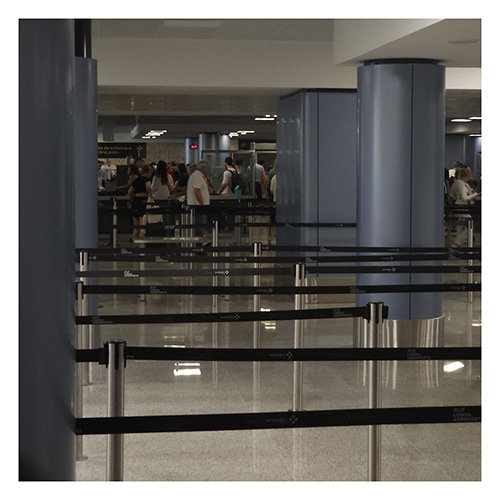 Absperrbänder zeihen sich durch eine leere Wartehalle vor dem Check-In. Am Check-In sind einige Passagiere zu sehen.